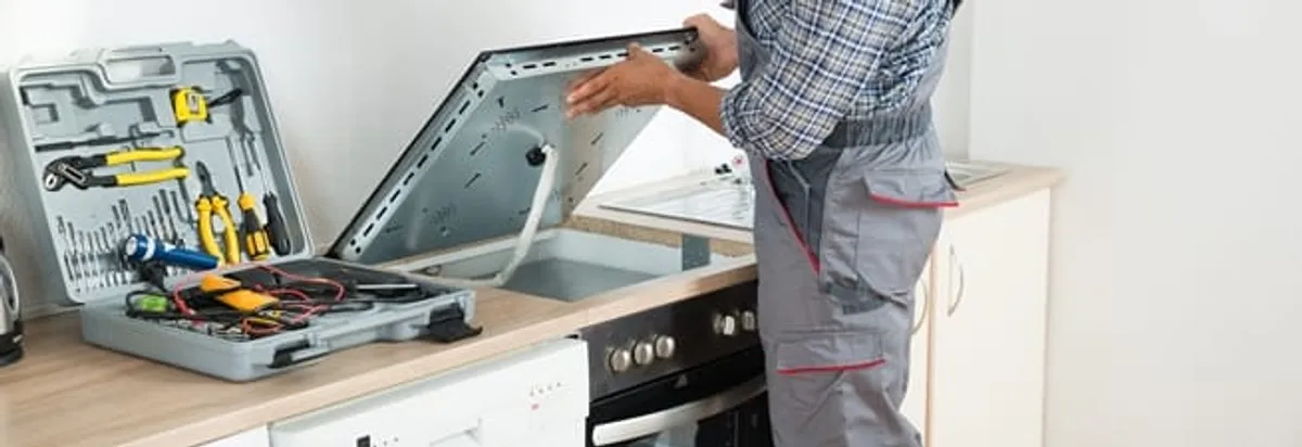 Cooktop repair technician lifting a built-in stovetop for service in Knoxville, TN