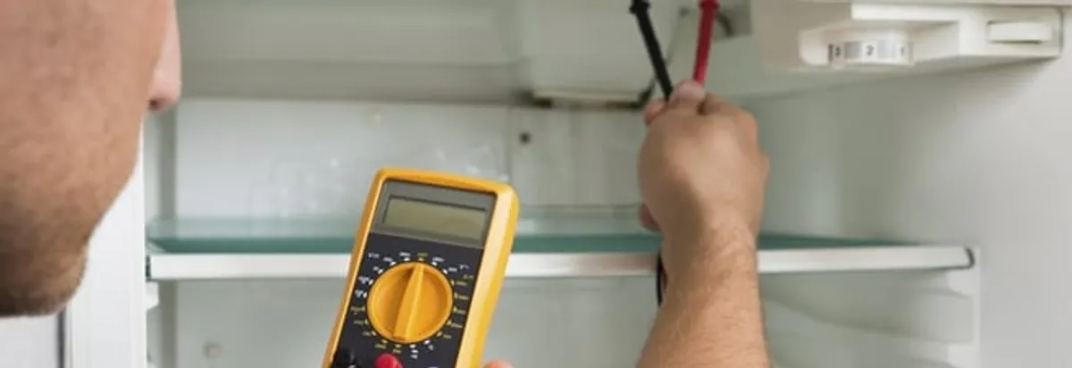 Refrigerator repair technician testing electrical components with a multimeter in Knoxville, TN